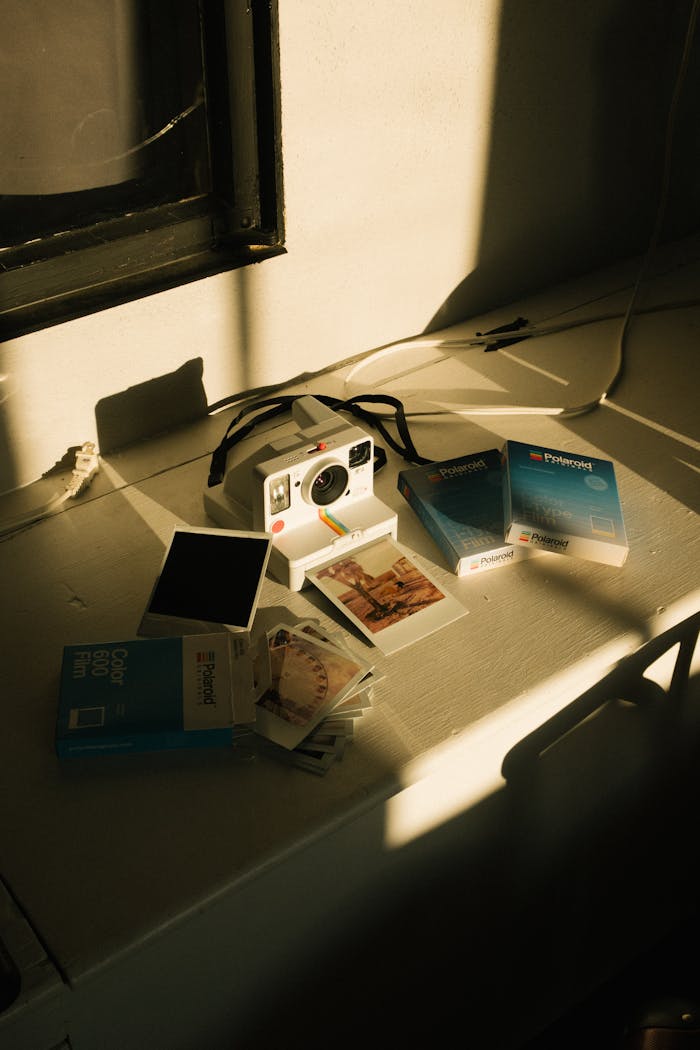 A vintage instant camera set on a sunlit desk with film packs and photographs.