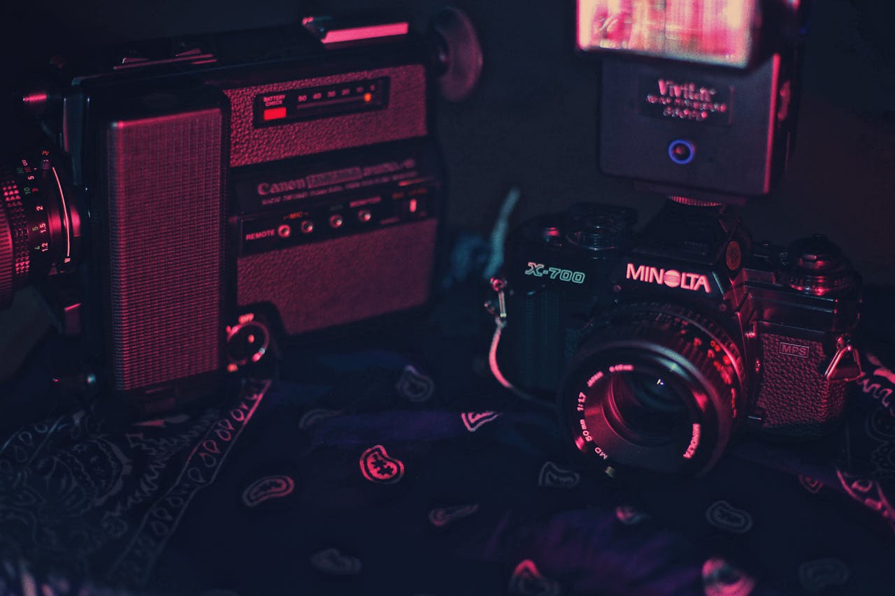 Vintage Minolta film and Canon video cameras displayed in a dimly lit studio.