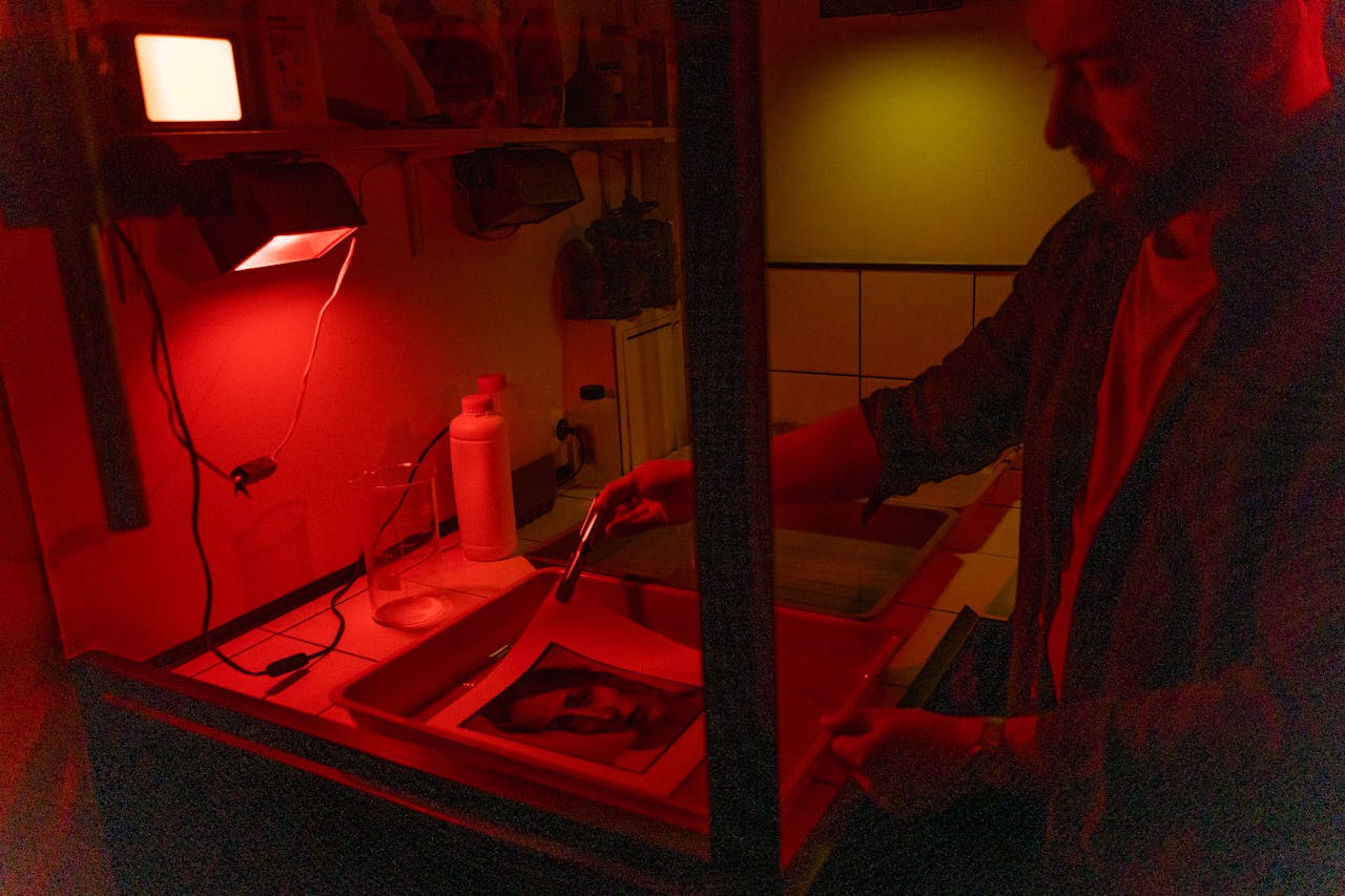A photographer develops film in a darkroom under red light, showcasing the classic processing method.